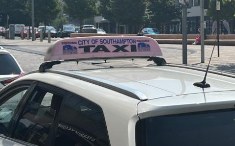 The roof of a white Southampton taxi on a rank, with a mounted Southampton City Council licence plate