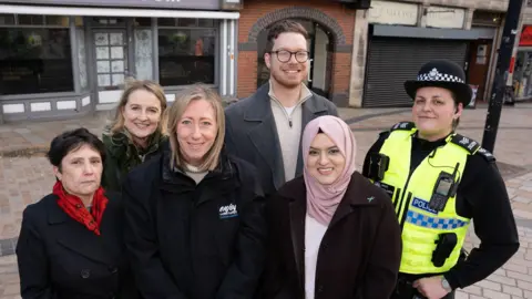 A group of five women and one man, including a woman in a police uniform on the right. They are stood on Queen Street in Wolverhampton city centre