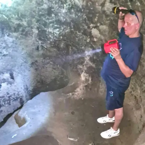 Janine Tanner A man in holding two torches, which illuminate a cave, with a set of rough stone steps leading down