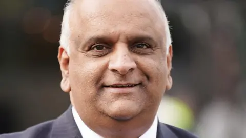 Head and shoulders image of councillor Azhar Ali. He is smiling, has short white hair and is wearing a white shirt and grey striped suit jacket