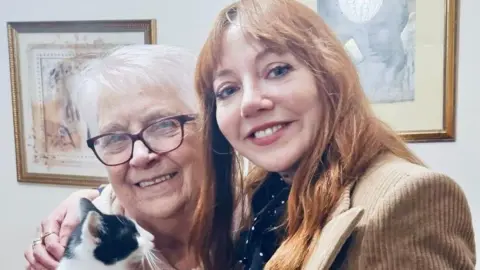 Moggies Cat Rescue Doreen Miller and Diane Morgan standing side by side. Morgan has her arm around Doreen Miller who is holding a cat
