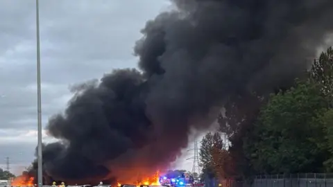 Thick black smoke rises from a fire at a car storage compound