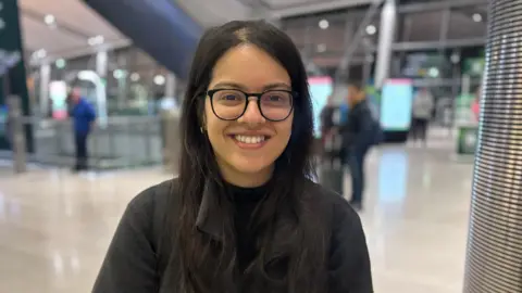 Rushali Lakhani has long dark hair and black glasses. She is wearing a black top.