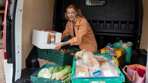 Getty Images Relawan melihat ke kamera sambil tertawa sambil menurunkan mobil van berisi makanan ke dalam nampan untuk bank makanan. Dia berada di Timur Laut Inggris dan senang bisa berkontribusi kembali kepada komunitasnya.