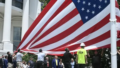 Trump surrounded by family looks up at large American flag getting installed at the White House