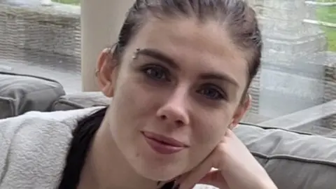 Holly Collinson is seen with her hair scraped back, an eyebrow earring and she smiles toward the camera. 