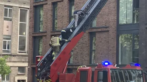A firefighter helps two men down a ladder from a tower block in the centre of Bristol