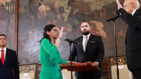 Getty Images Delcy Rodríguez wears a green dress and places her left hand on a red velvet covered book as she raises her right hand and is sworn in as interim president 