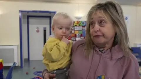Hayley Rich in a violet hoodie, holding a toddler with blond hair in her arm