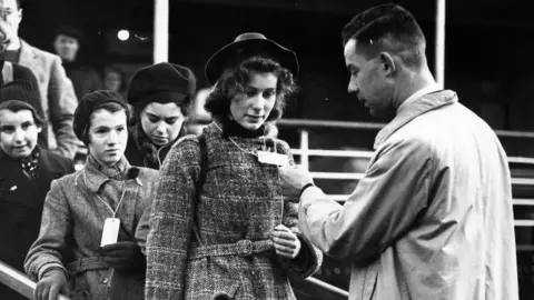 Central Press/Getty Images Young woman's identify tag is checked as she leaves a boat at Harwich, Essex, on 2 December 1938