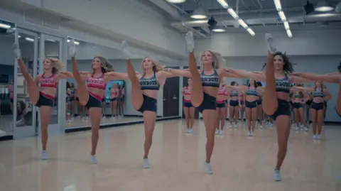 Netflix Cheerleaders doing high kicks in a row in a dance studio 