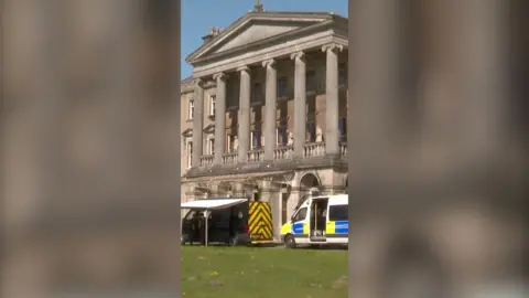 A stately manor with police vans in front