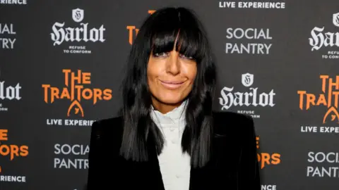 Getty Images Claudia Winkleman is looking into the camera. A backdrop saying the traitors is behind her. She has black bobbed hair and a fringe. 