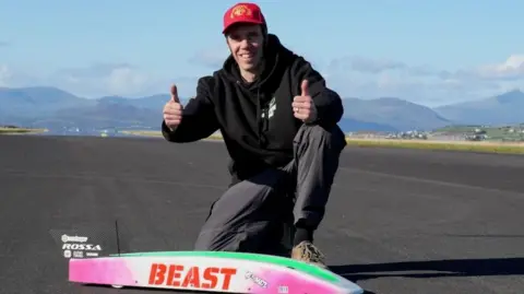 man kneeling on tarmac in front of him a remote control car.