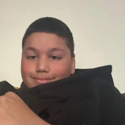 PA Media Reece Khan - a boy with short black hair - sat in a black hoodie.