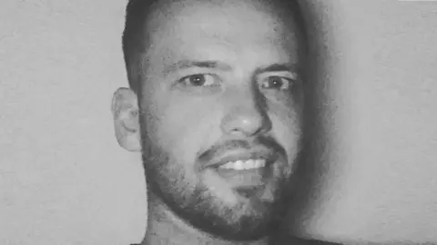 Spindrift Black and white headshot of a grinning man with short dark hair and a well trimmed beard and moustache. 
