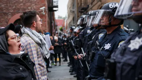 Reuters A line of protesters stand facing a line of police in riot gear in San Francisco on 9 June 2025