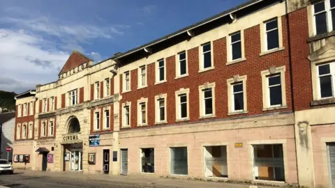 An old cinema building with a brick faced and the name Pavilion above the entrance with a blue sky overhead