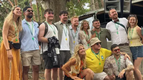 George King/BBC A group picture of men and women all smiling together. There are trees in the background.