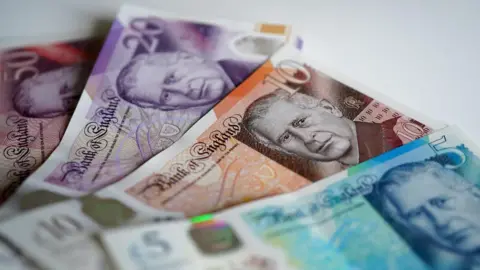 Banknotes of £5, £10, £20 and £50 fanned out on a white surface