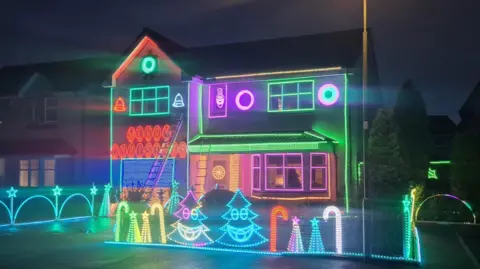 Gary Gray A two-storey house brightly illuminated in multi-coloured Christmas lights. There are small light up Christmas trees and light up candy canes around the border of the garden. 