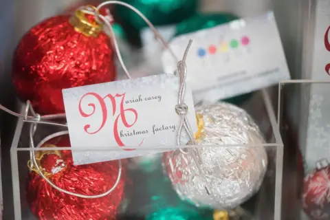 Getty Images A shop display shows red and silver Christmas Tree ornaments, with a tag that reads "Mariah Carey Christmas Factory"