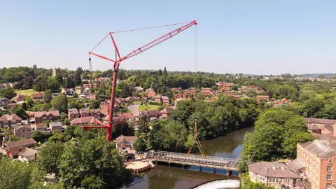 A large red crane lifting a metal bridge from its place