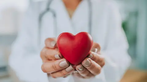 A picture of a female doctor holding a plastic red heart.