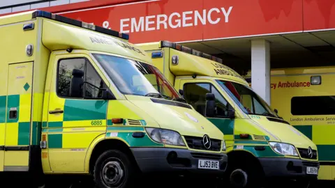 Two emergency ambulance vehicles are parked outside a red sign reading 'Accident & Emergency' at the A&E ward at St Thomas' Hospital in London in 2015.