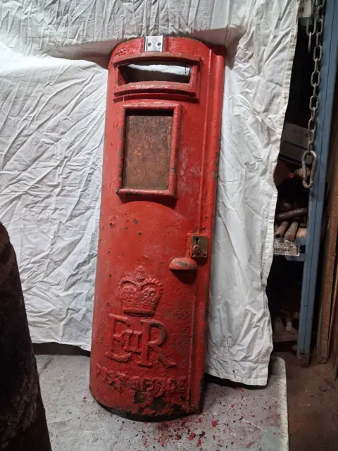 Jay Anderson The rusted front of a postbox in a workshop