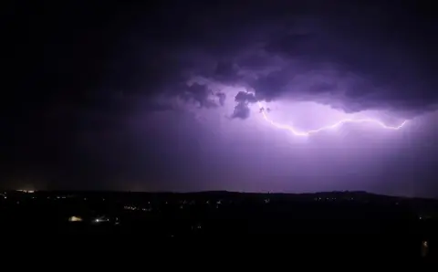 Colby Taylor A bright shaft of lightning striking ground illuminates a dark night sky