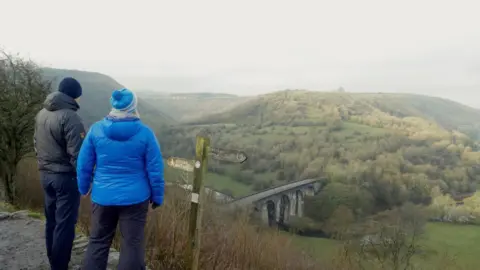 Peak District National Park Two people with their back to the camera at the Monsal Trail enjoying a view of the Peak District.