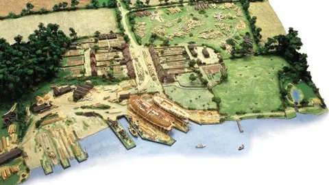 Beaulieu Enterprises Ltd Image shows a model of how Buckler's Hard looked whilst ships were being built. It shows the slipways where ships were built. It shows the village surrounded by fields. There are a number of logs and wood placed around the village.