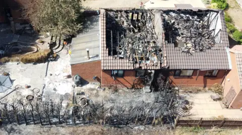 John Fairhall/BBC An aerial drone photograph of Siobhan's bungalow. Where conifer trees once stood they have now been singed from the fire and the roof has caved in.