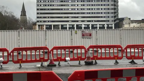 Barriers and signage surrounding a building site with one red and white sign clearly stating "demolition in progress".