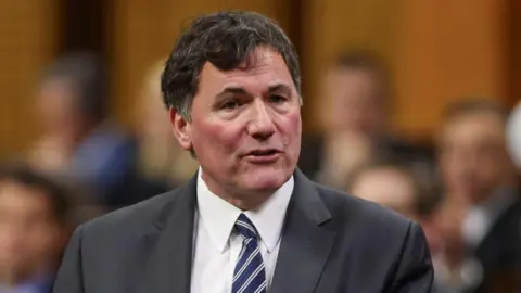 Reuters Dominic Leblanc, mengenakan jas abu-abu, kemeja putih dan dasi bergaris, berbicara di House of Commons. 