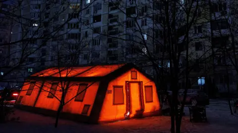 Reuters The tent of a government-run humanitarian aid point is lit up orange during a power outage in Kyiv.