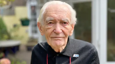 John Farago, an elderly man with white hair, wearing a black top