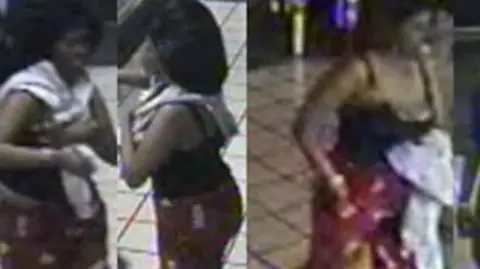 British Transport Police Blurred CCTV images of a woman in a London underground station who is wearing a black top and red patterned trousers.