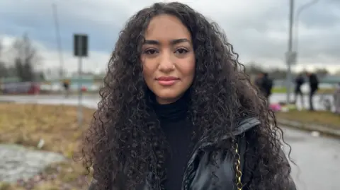 Woman with black curly hands faces camera in black puffy jacket