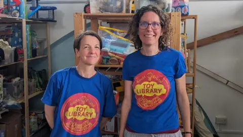 BBC Volunteers Stacy Yelland (L) and Ava Lorenc in front of rows of toys