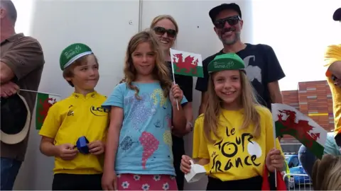 Family of two parents and three children wearing yellow and holding Wales flags