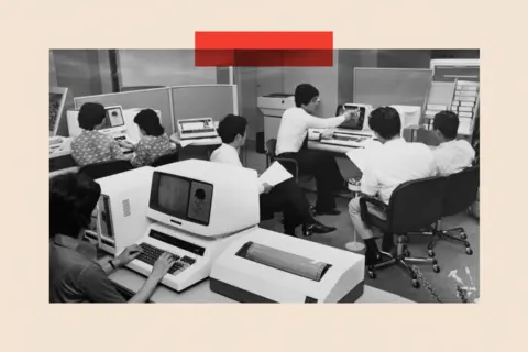 Getty Images A black-and-white image of office workers sitting around working, in Japan