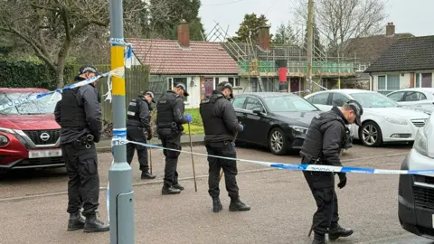 BBC Four police officers in uniform in a line holding sticks looking for evidence as they move along a road on a residential street