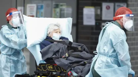 EPA Healthworkers wearing full protective equipment wheel out an elderly patient