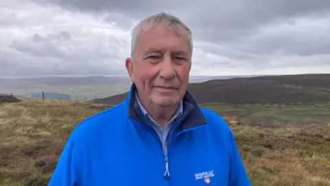 Carla Fowler/BBC A picture of Earl Parker in front of the Yorkshire Dales National Park, smiling wearing a blue zip up fleece 