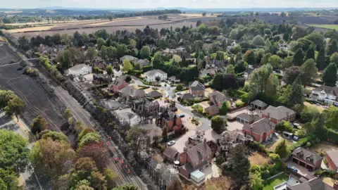 An aerial view of the devastation that wildfires have taken on an area of Stourbridge. Several houses are blackened or destroyed, with a field behind the houses completely black.