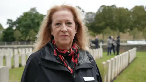 Tracey Bowers looking at the camera with war graves behind her