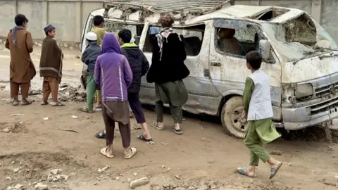 People look at a wrecked vehicle in Baghlan province