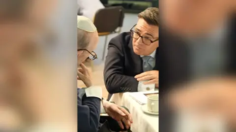 Younger man in suit listening attentively to an elderly man wearing a kippah